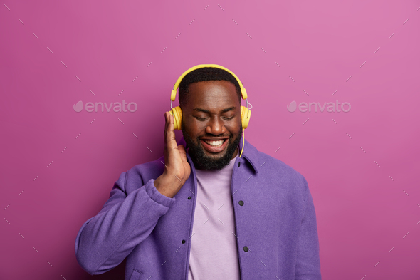 Smiling black man enjoys good sound in headphones, made new playlist, listens favourite music during