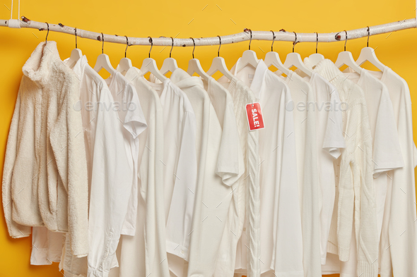 Clearance sale of white clothes on hangers isolated over yellow background.  Selection of fashion gar Stock Photo by wayhomestudioo