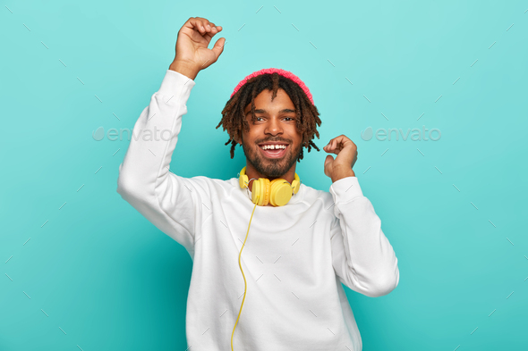 Upbeat carefree mixed race guy dances with hands up, listens awesome music track via headphones, has