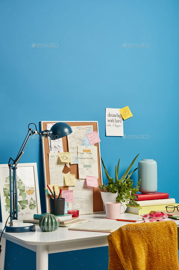Cozy workplace with notebooks, beverage, desk lamp and different notes on wall near, reminding what