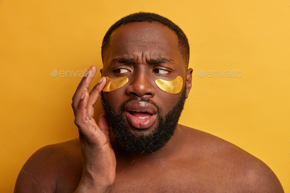 Headshot of black man applies cosmetic sponges under eyes, removes wrinkles, has thick bristle, stan