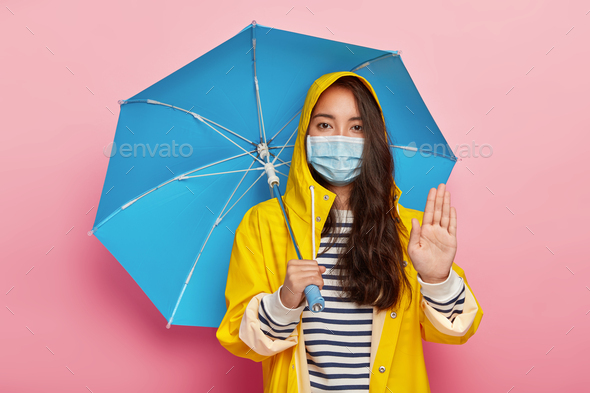 Serious girl makes stop gesture, asks not pollute environment, walks in acid rain, wears protective