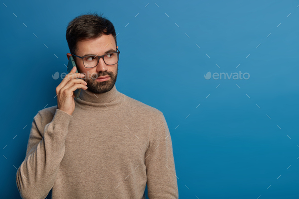 Photo of serious bearded young guy talks on phone, calls someone via modern gadget, expresses seriou