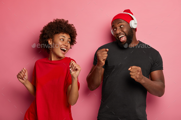 Image of amused dark skinned female and male enjoy listening favourite track list, dance with rhythm