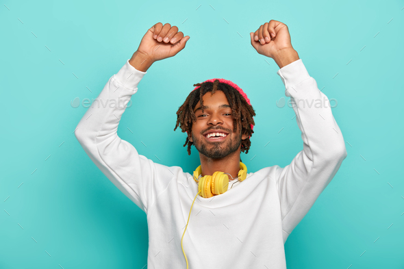 Photo of energetic dark skinned guy has dread hair, lifts hands up, dances lively and smiles broadly