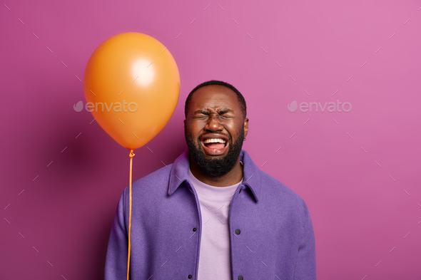 Dissatisfied black man cries, being alone on holiday, feels lonely, holds balloon upset guests didnt