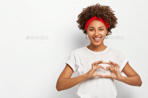 Love to you, my dear. Glad satisfied African American woman makes heart gesture, smiles pleasantly a
