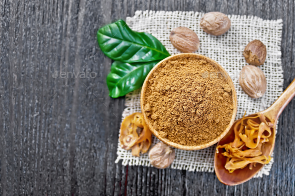 Nutmeg round in bowl and mace in spoon on dark board top - Stock Photo - Images