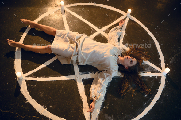 Demonic woman lying in magic circle with candles