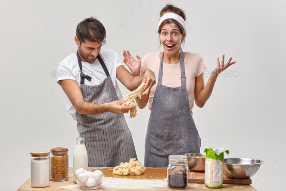 Hard working man in apron practices baking skills together with wife, try to make dough for pastry o - Stock Photo - Images