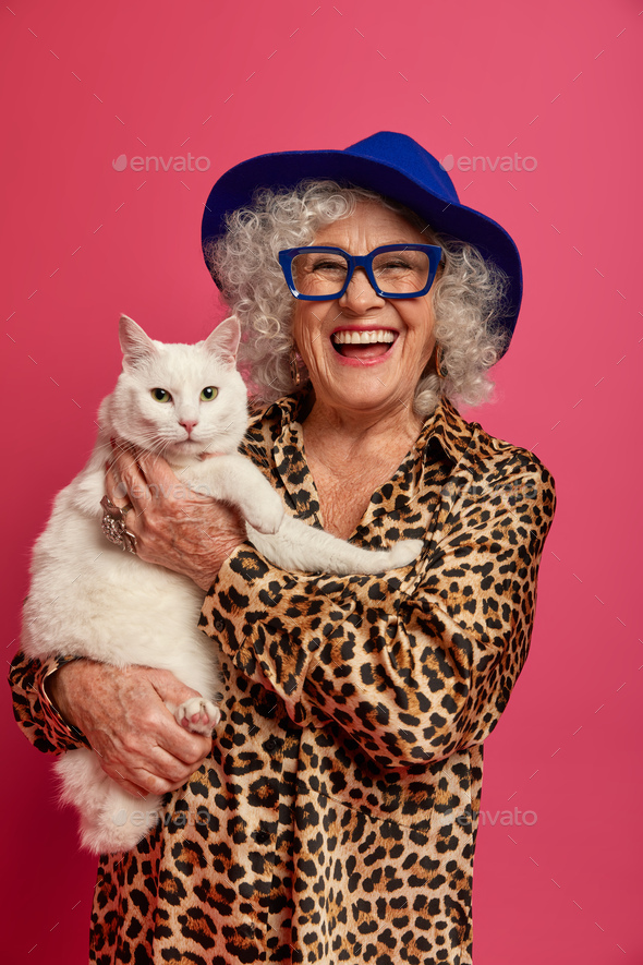 Vertical image of fashionable elderly woman wears hat, leopard outfit, optical glasses, smiles posit