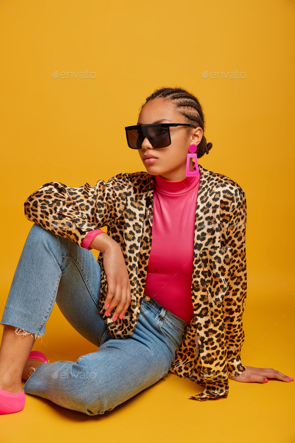 Vertical shot of fashionable dark skinned woman with cornrow hairstyle, wears big trendy sunglasses,