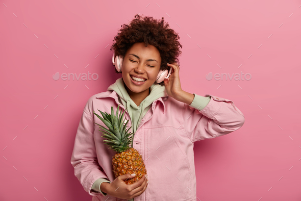 Indoor shot of cheerful millennial girl listens music and enjoys great sound in headphones, bought f