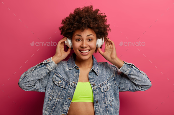 Energetic dark skinned smiling woman being on positive tune, listens songs from playlist in stereo h