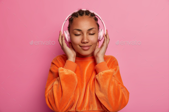 Pleased relaxed calm young woman with dark skin closes eyes, enjoys music application, pefect sound,