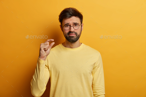 Disappointed adult man shows small size, measures something very tiny with fingers, shows insufficie - Stock Photo - Images