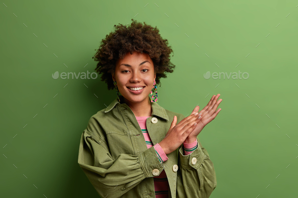 Positive mysterious woman smiles toothily, rubs palms with intention to make dream real, enjoys good