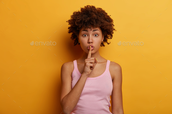 Photo Of Surprised Curly Woman Keeps Secret And Asks For Silence Presses Index Finger To Lips