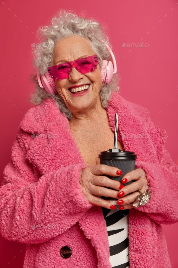 Joyful of fashionabele senior woman wears pink sunglasses and fur coat, has red manicure and makeup,