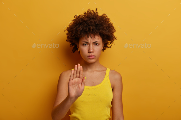 Beautiful serious young woman pulls hand towards camera in stop gesture, asks to calm down and stop