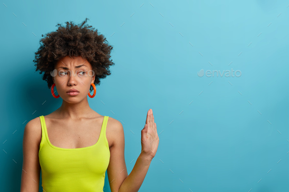 Serious dissatisfied woman with curly hair makes stop gesture, pulls palm forward away, asks not to