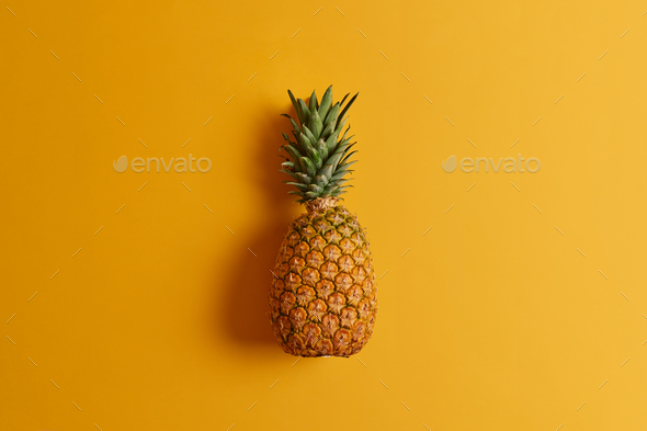 Ripe pineapple isolated on yellow background. Exotic fruit low in calories, loaded with nutrients an