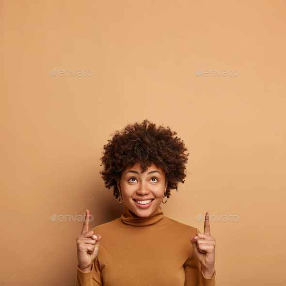 Vertical image of good looking Afro American woman with curly hairstyle, grabs your attention to som