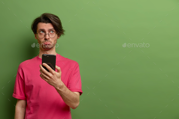 Upset dissatisfied European man holds smartphone with sad expession, finds out someone spreading rum