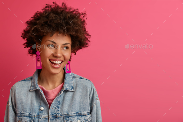 Lucky stylish woman with Afro hairstyle looks aside, smiles positively, enjoys life, being amused by