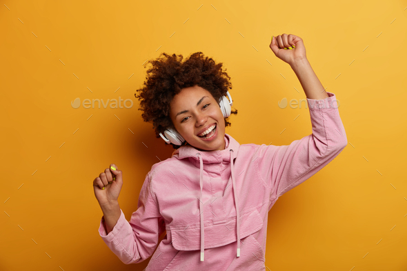 Joyful carefree woman dances to music, listens favourite audio track, raises hands with clenched fis