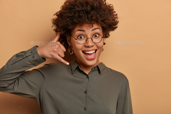 Whos calling? Positive Afro American woman imitates phone call, makes mobile gesture and waits for a