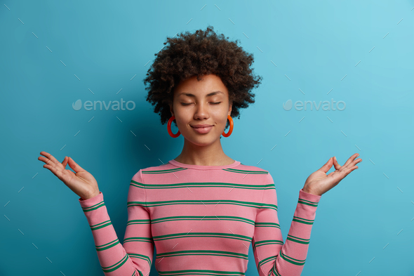 Calm curly haired young woman does meditation gesture, finds harmony in ...