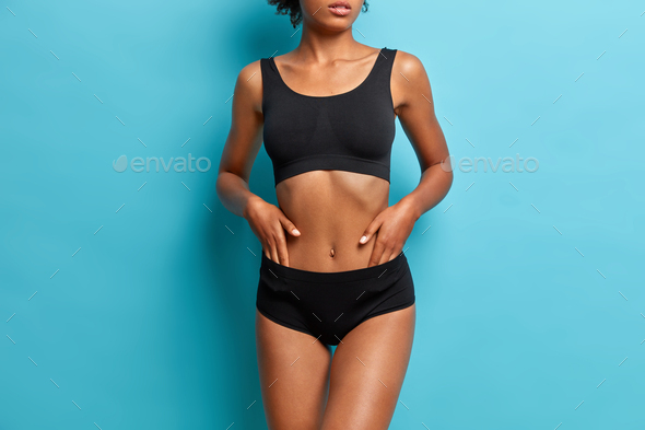 Sporty dark skinned woman demonstrates results after fitness training dressed in black cropped top a