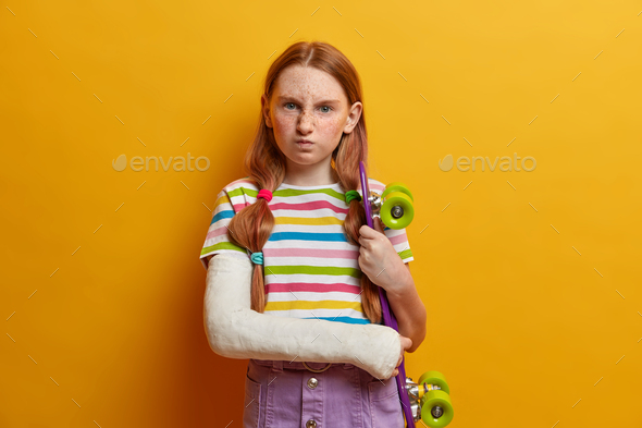 Annoyed little girl with ginger hair and freckles, smirks face and has dissatisfied expression, pose