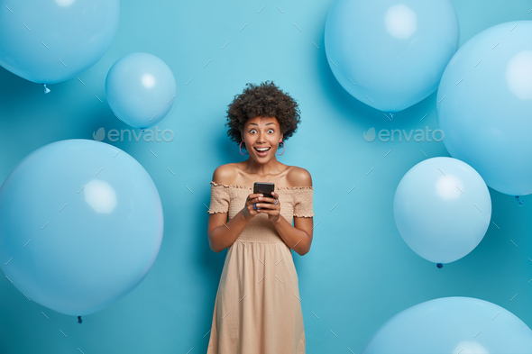 Positive glad African American woman holds mobile phone in hands and happy to chat with friends in s