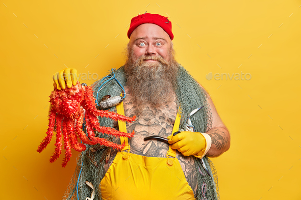 Funny blue eyed seaman holds big octopus and smoking pipe, leads seafaring life, dressed in sailor c