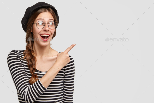 Cheerful young female French teacher shows happily something to students, indicates with index finge