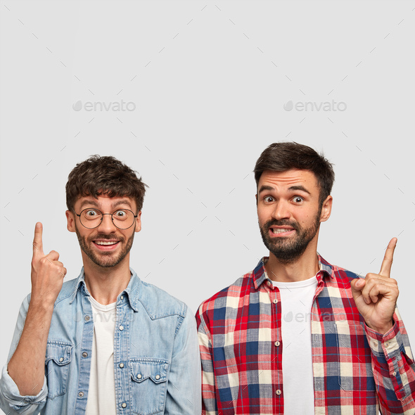 Optimistic young male companions point upwards, happy to advertise something pleasant, show blank sp
