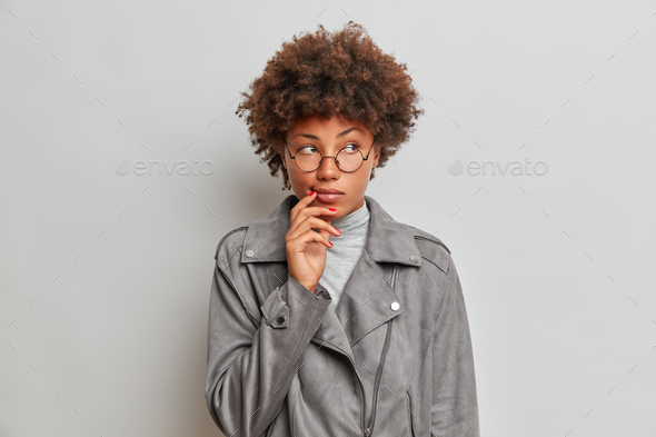 Thoughtful beautiful young Afro American woman with curly hairstyle takes decision in mind, remember