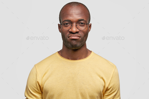 Indoor shot of displeased African American dark skinned male frowns face as being in low spirit, rec