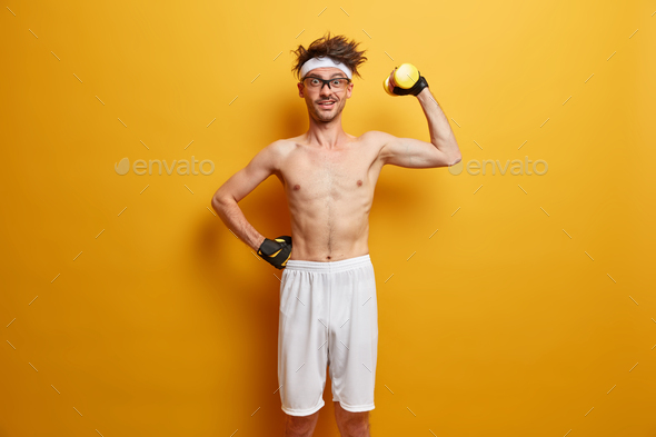 Indoor shot of positive man holds heavy sport equipment, enjoys workout in own gym, has skinny body,