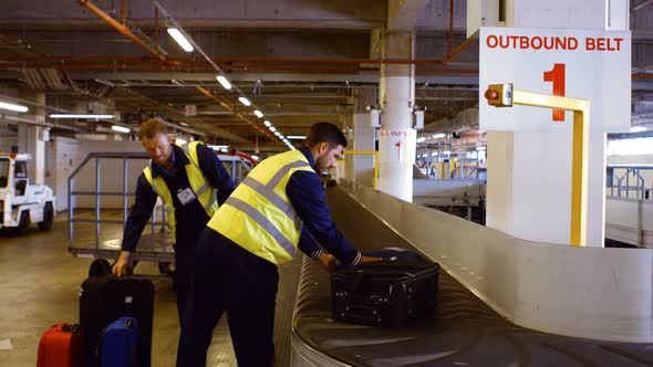 Two airport workers putting baggage on baggage carousel alt