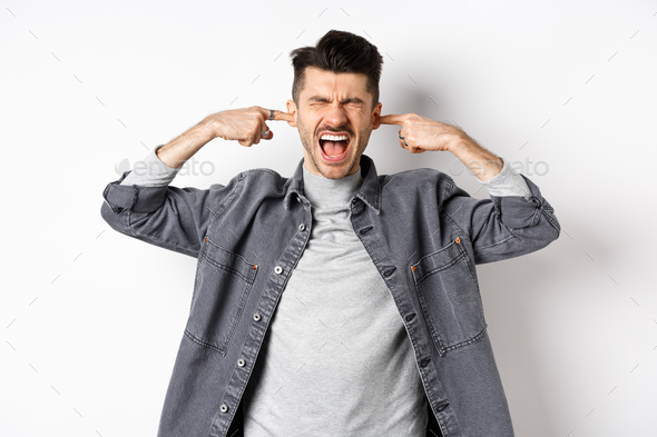 Annoyed guy shut ears and screaming, displeased by loud noise, yelling to stop noisy music, standing - Stock Photo - Images