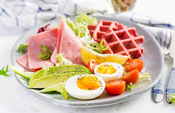 Breakfast with beetroot waffles, boiled egg, ham, tomato and slice avocado