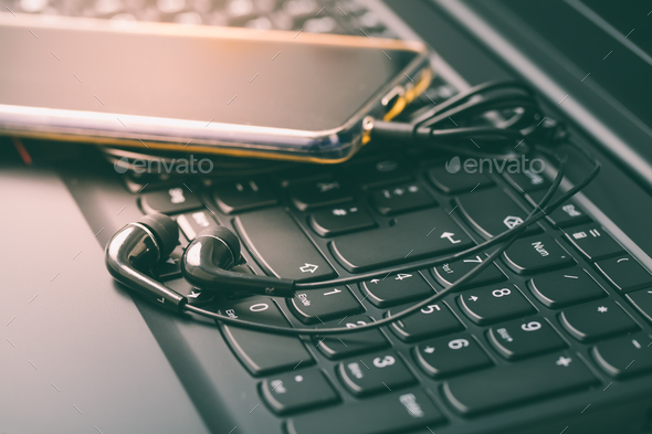 Black earphones with smart phone on keyboard in black - Stock Photo - Images