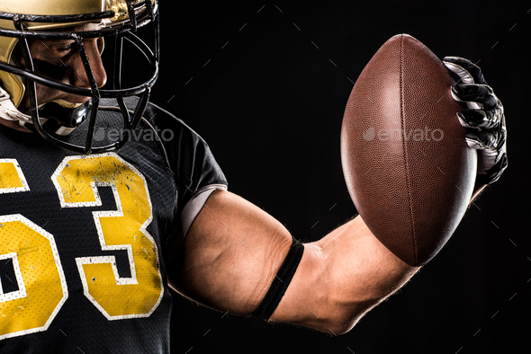Muscular american football player in protective sportswear looking at ball