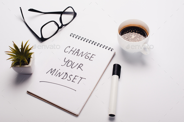 notebook with change young mindset inscription, felt-tip pen, coffee cup, glasses and potted plant