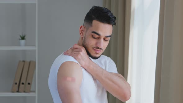 Happy Handsome Arabic Male Patient Wearing White Tshirt Points to Shoulder at Injection Mark Sealed alt