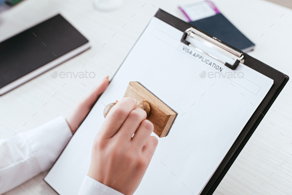 selective focus of female lawyer with stamp in hand holding clipboard with visa application