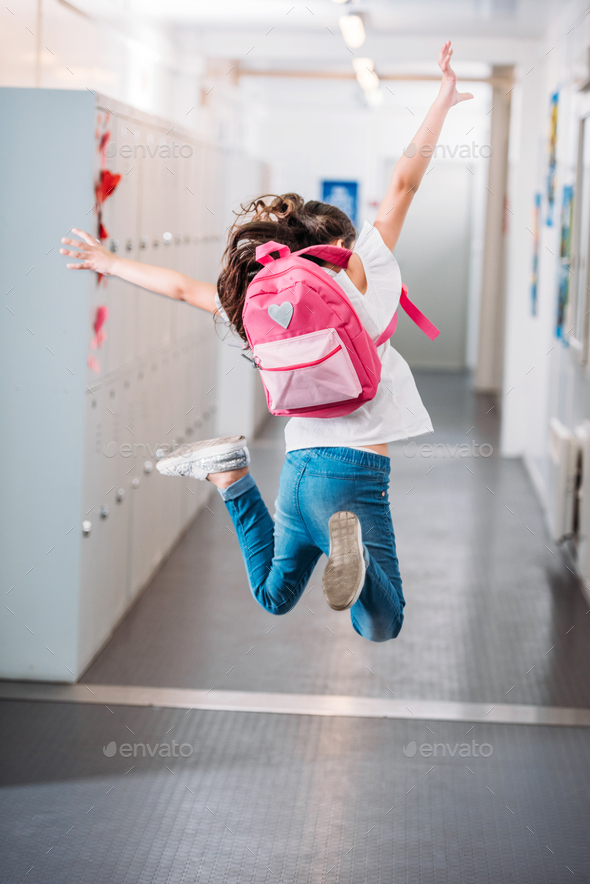 back view of girl jumping in school corridor with raised hands